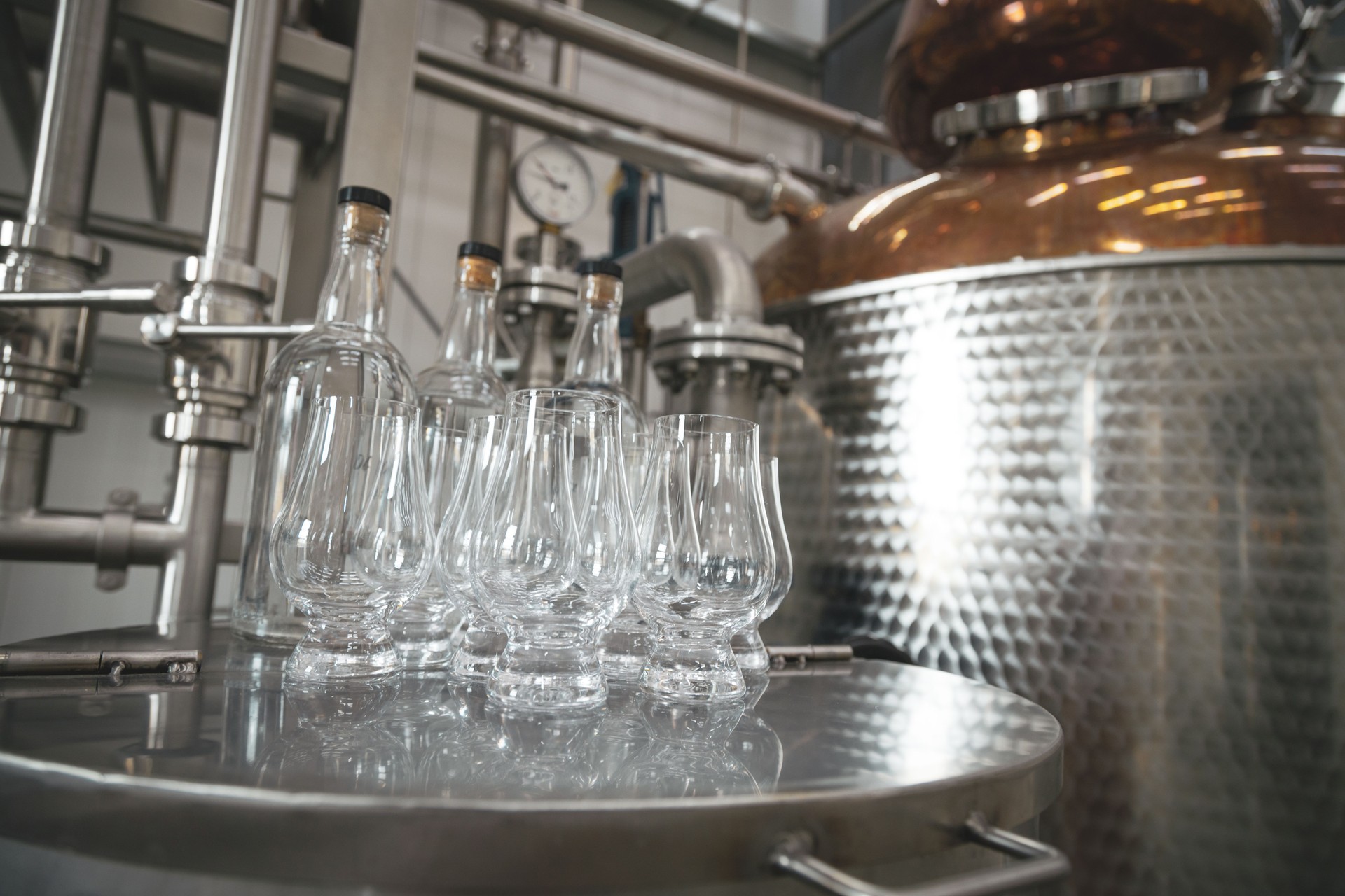 Modern distillery equipment. Industrial equipment for whisky production.  Glasses for whisky degustation in front of copper vacuum still.
